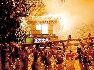 A portable shrine wildly swung by men under cascades of fireworks sparks.